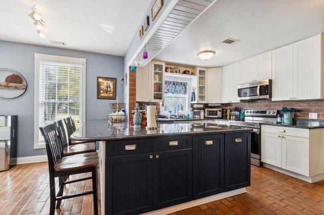 kitchen featuring visible vents, a kitchen bar, brick floor, white cabinets, and stainless steel appliances