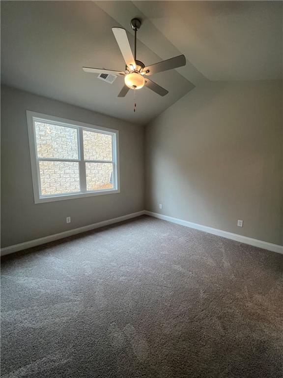 carpeted spare room with ceiling fan and vaulted ceiling