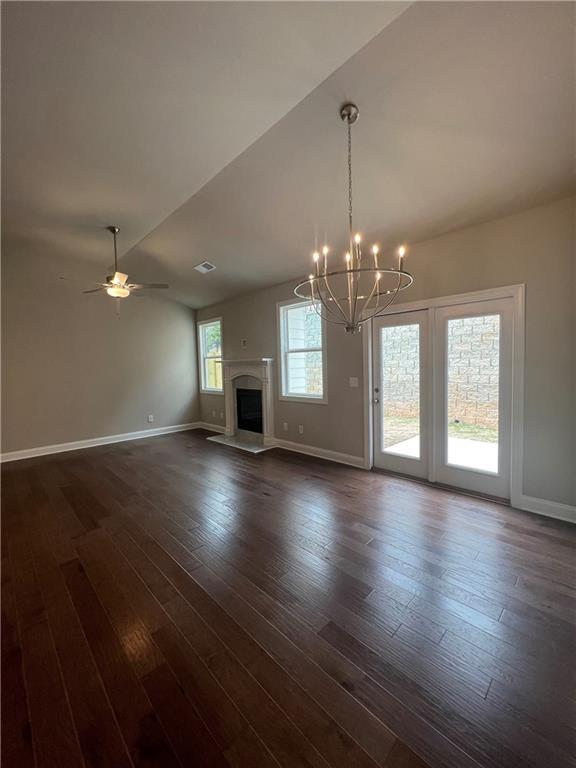 unfurnished living room featuring ceiling fan with notable chandelier, vaulted ceiling, and dark wood-type flooring