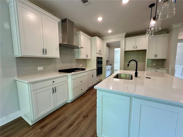 kitchen with wall chimney range hood, stainless steel gas stovetop, a sink, and dark wood-type flooring
