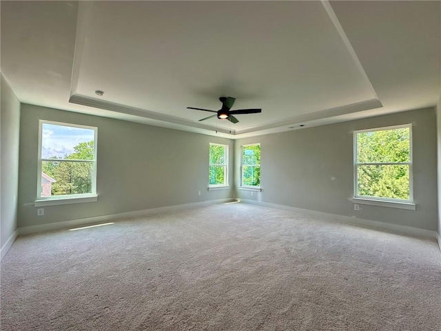 carpeted spare room featuring a raised ceiling, baseboards, and ceiling fan