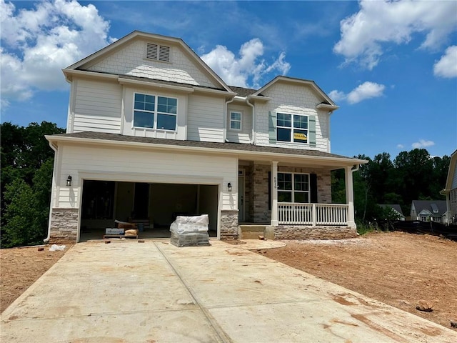 view of front of home with covered porch, an attached garage, driveway, and stone siding