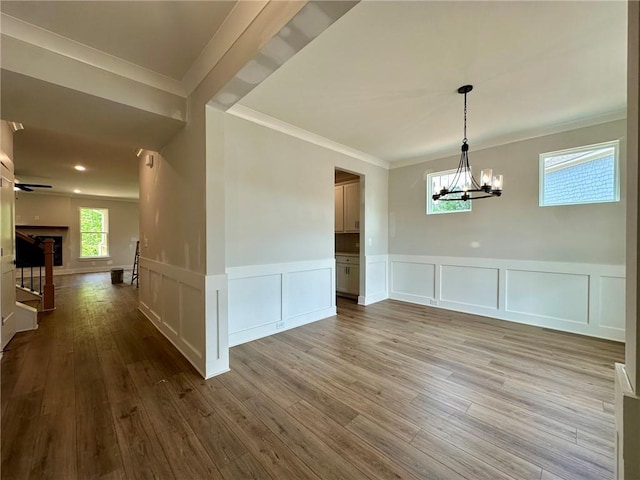 unfurnished dining area with ornamental molding, wainscoting, a decorative wall, wood finished floors, and a chandelier