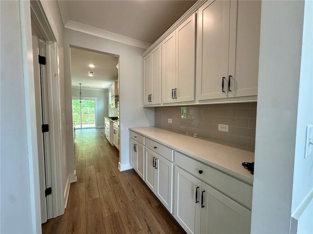 kitchen featuring crown molding, dark wood-type flooring, light countertops, white cabinetry, and tasteful backsplash