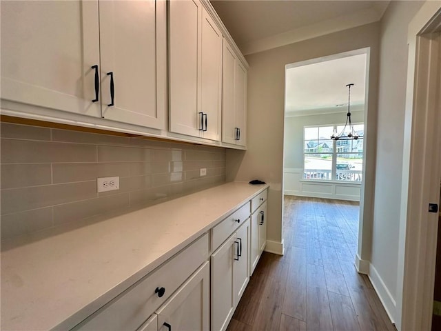 interior space with an inviting chandelier, dark wood-style flooring, baseboards, white cabinets, and backsplash
