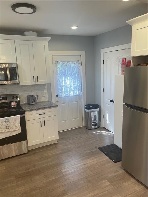 kitchen with backsplash, white cabinetry, hardwood / wood-style floors, and stainless steel appliances