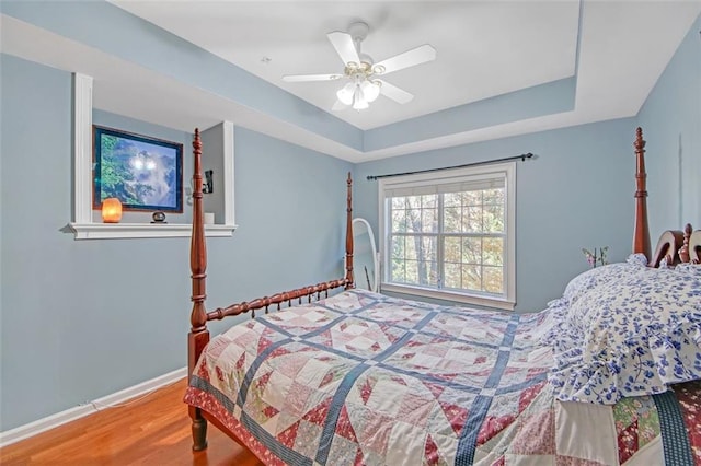 bedroom featuring hardwood / wood-style floors, ceiling fan, and a raised ceiling