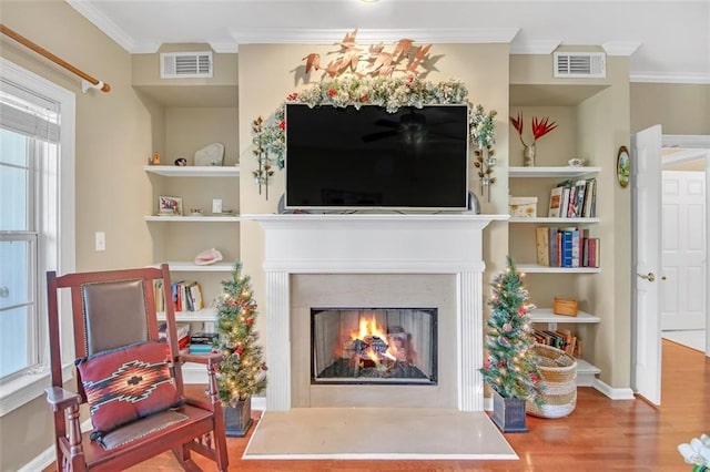 sitting room with built in shelves, crown molding, and hardwood / wood-style floors