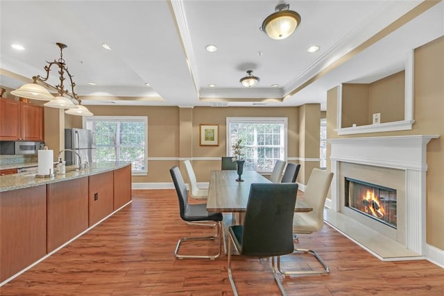 dining area with a tray ceiling, crown molding, light hardwood / wood-style floors, and sink