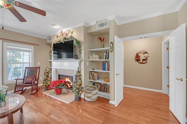 living room with built in shelves, ceiling fan, ornamental molding, and light wood-type flooring