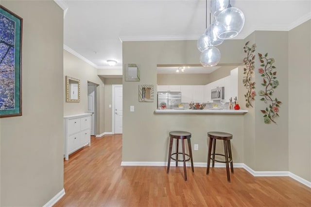 kitchen with a kitchen bar, appliances with stainless steel finishes, crown molding, white cabinets, and light hardwood / wood-style floors