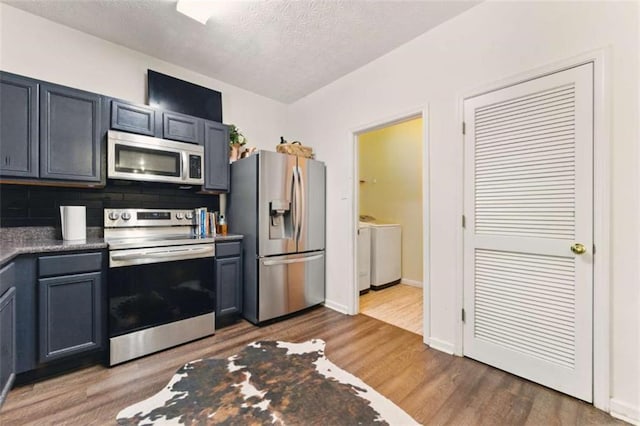 1689 Camden Forrest Way, Riverdale, GA 30296 - kitchen with appliances with stainless steel finishes, washer and clothes dryer, wood finished floors, a textured ceiling, and backsplash