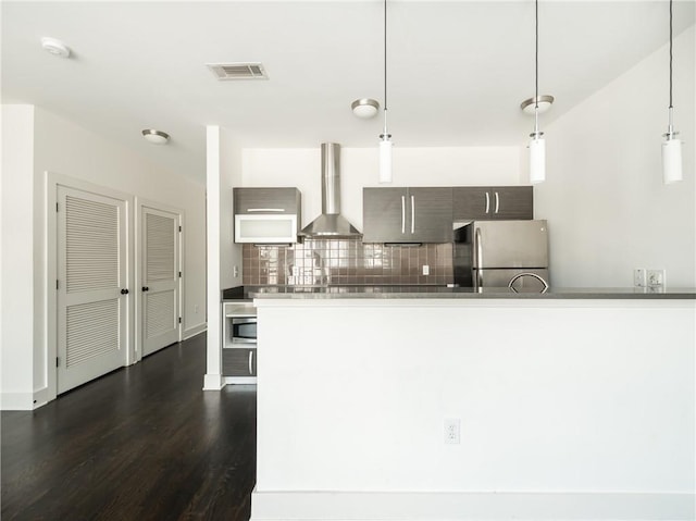 kitchen with hanging light fixtures, wall chimney range hood, tasteful backsplash, dark hardwood / wood-style floors, and appliances with stainless steel finishes