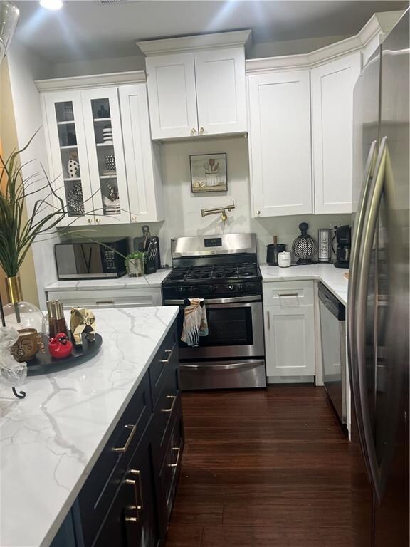 kitchen with dark wood-type flooring, light stone countertops, stainless steel appliances, and white cabinetry