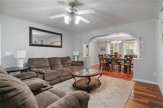 living area with arched walkways, baseboards, ceiling fan with notable chandelier, and wood finished floors