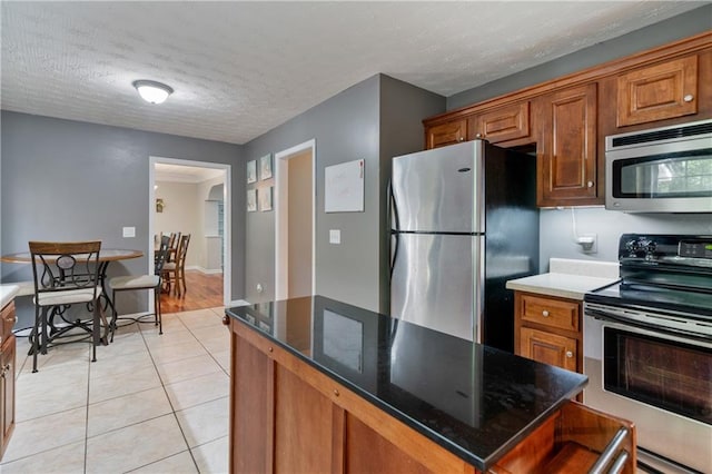 kitchen featuring brown cabinetry, a kitchen island, a textured ceiling, appliances with stainless steel finishes, and light tile patterned flooring