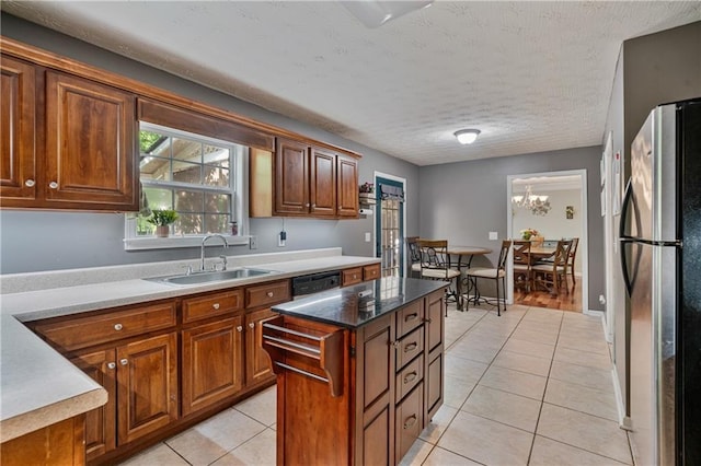 kitchen with light tile patterned flooring, a sink, brown cabinetry, a center island, and freestanding refrigerator