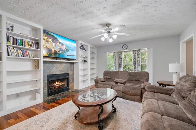 living area with a textured ceiling, ceiling fan, a fireplace, and wood finished floors