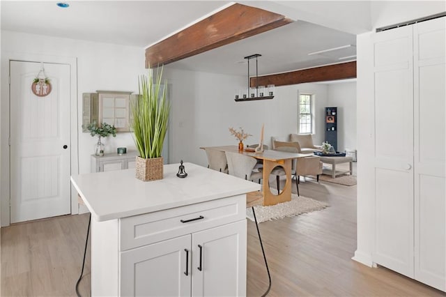 kitchen with beamed ceiling, a center island, decorative light fixtures, and white cabinetry