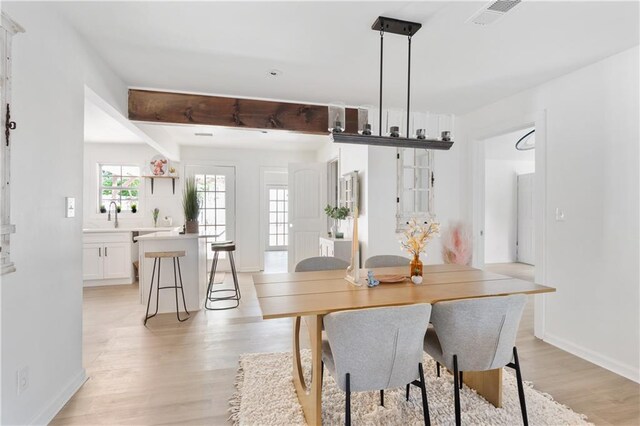 dining room featuring sink, beamed ceiling, and light hardwood / wood-style floors