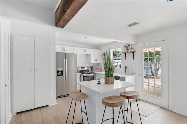 kitchen with appliances with stainless steel finishes, a kitchen breakfast bar, light hardwood / wood-style flooring, beamed ceiling, and white cabinetry