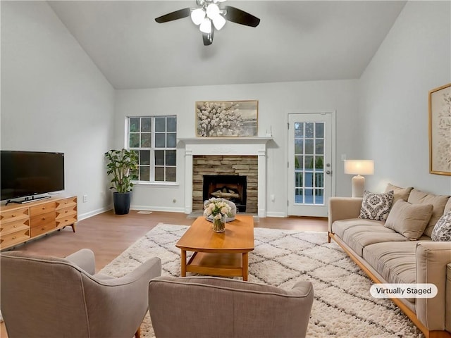 living room with ceiling fan, a stone fireplace, light wood-type flooring, and vaulted ceiling