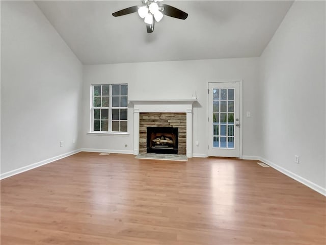 unfurnished living room featuring light wood-type flooring, a stone fireplace, ceiling fan, and vaulted ceiling