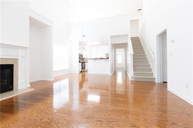 3277 Wyesham Cir, Duluth, GA 30096 - unfurnished living room with a towering ceiling, light wood-type flooring, stairs, a high end fireplace, and baseboards