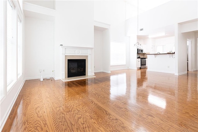 3277 Wyesham Cir, Duluth, GA 30096 - unfurnished living room featuring light wood finished floors, a high ceiling, a high end fireplace, healthy amount of natural light, and baseboards