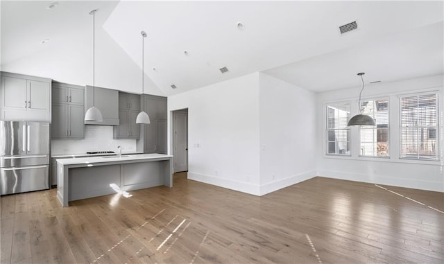 kitchen with stainless steel refrigerator, dark hardwood / wood-style floors, backsplash, gray cabinets, and a center island with sink