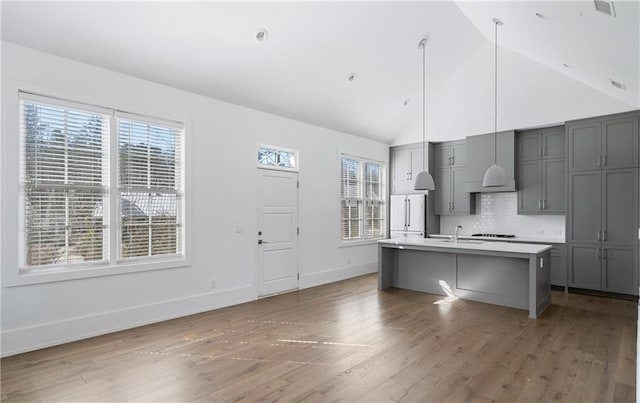 kitchen featuring dark hardwood / wood-style flooring, tasteful backsplash, gray cabinetry, hanging light fixtures, and an island with sink