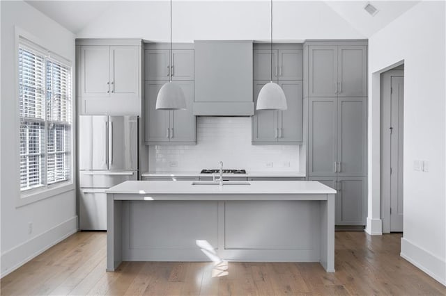 kitchen featuring vaulted ceiling, gray cabinets, and stainless steel refrigerator