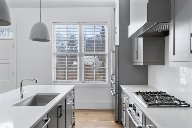 kitchen with sink, wall chimney exhaust hood, stainless steel appliances, tasteful backsplash, and decorative light fixtures