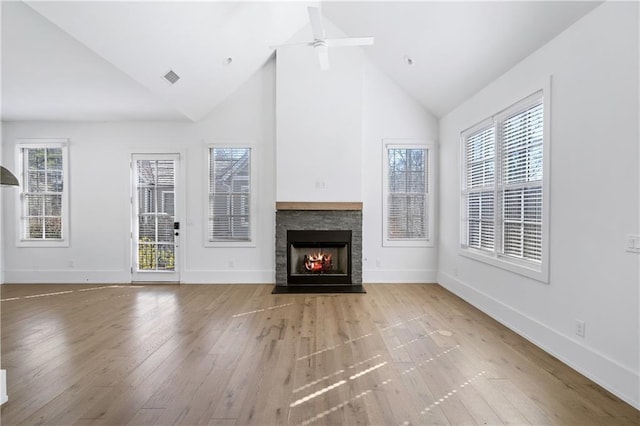 unfurnished living room with ceiling fan, light hardwood / wood-style floors, a stone fireplace, and high vaulted ceiling