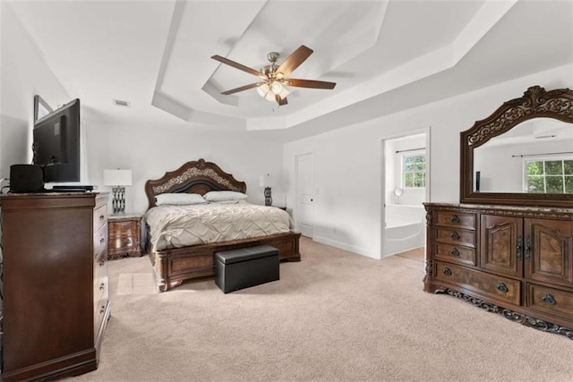 bedroom with multiple windows, connected bathroom, a tray ceiling, and light carpet