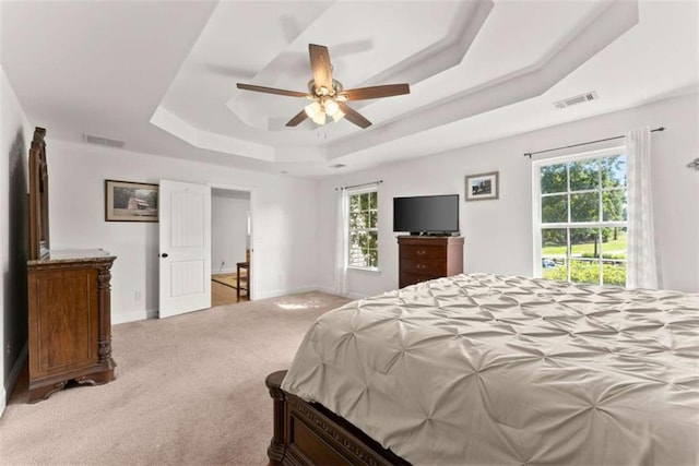 carpeted bedroom with a raised ceiling and ceiling fan