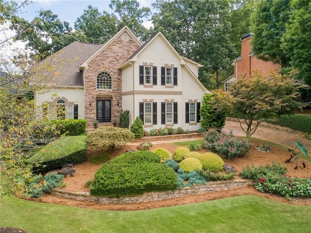 view of front facade with a front lawn, stone siding, french doors, and stucco siding