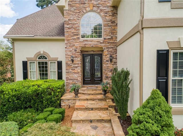 view of exterior entry featuring stone siding, french doors, a shingled roof, and stucco siding