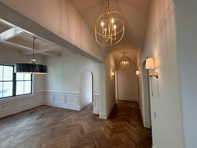 interior space featuring beam ceiling, arched walkways, wainscoting, baseboards, and a notable chandelier