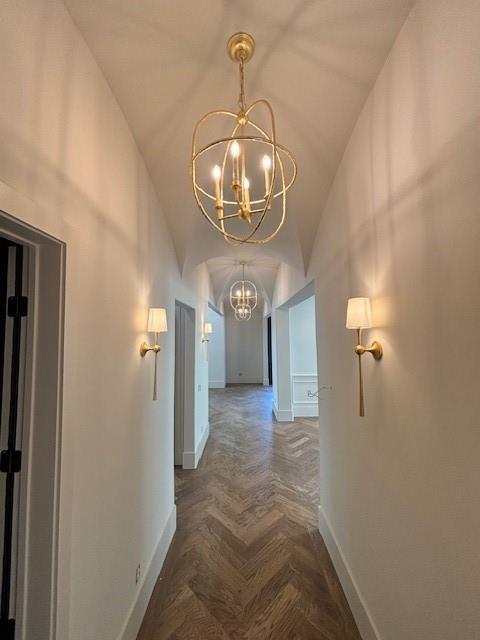 hallway with baseboards, a notable chandelier, and lofted ceiling