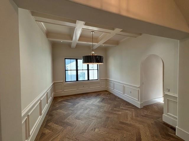 unfurnished dining area featuring wainscoting, a decorative wall, beam ceiling, and coffered ceiling
