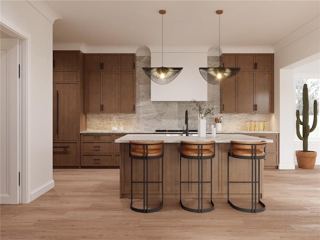 kitchen featuring a center island with sink, light countertops, crown molding, and light wood finished floors