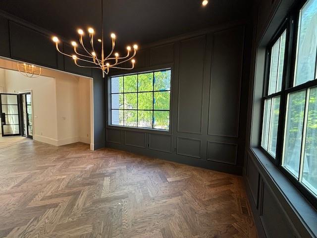 unfurnished room featuring plenty of natural light, a decorative wall, baseboards, and a notable chandelier