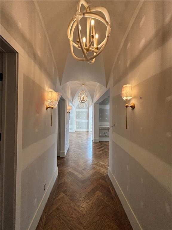 hall with a chandelier, arched walkways, vaulted ceiling, and baseboards