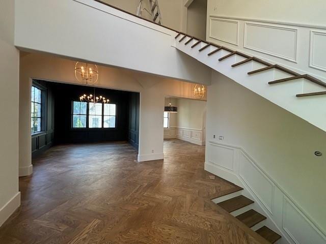 interior space with stairway, a decorative wall, an inviting chandelier, a wainscoted wall, and baseboards