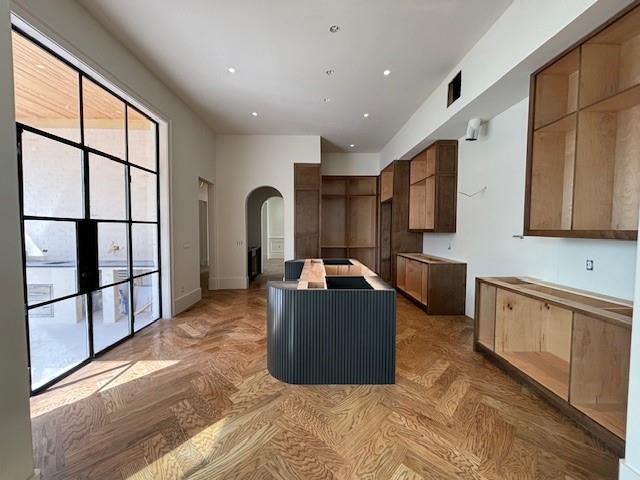 kitchen featuring arched walkways, a center island with sink, and recessed lighting