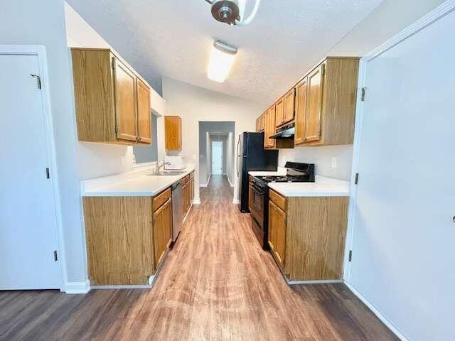 kitchen featuring hardwood / wood-style flooring, sink, vaulted ceiling, and black appliances