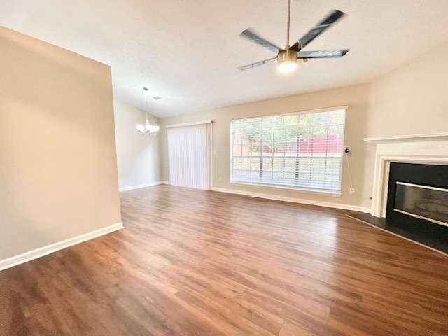 unfurnished living room featuring ceiling fan with notable chandelier, vaulted ceiling, and dark wood-type flooring