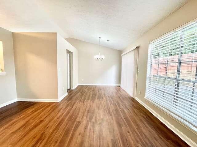 empty room featuring a textured ceiling, vaulted ceiling, dark wood-type flooring, and a chandelier