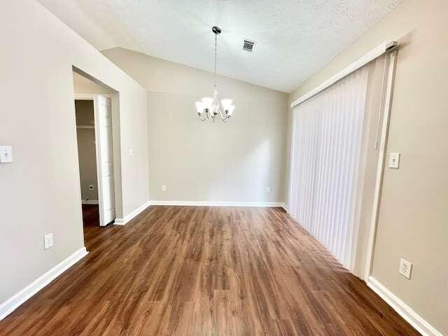 empty room with lofted ceiling, a textured ceiling, a chandelier, and dark hardwood / wood-style flooring